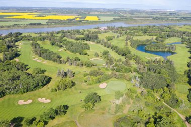 Arka planda göl olan golf sahası. Golf sahası ağaçlarla çevrili ve yeşil çimenli bir alanı var.