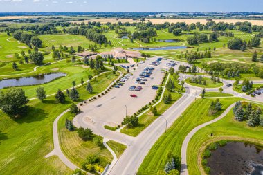 Otoparkı ve göleti olan bir golf sahası. Otopark arabalarla dolu ve gölet ağaçlarla çevrili.