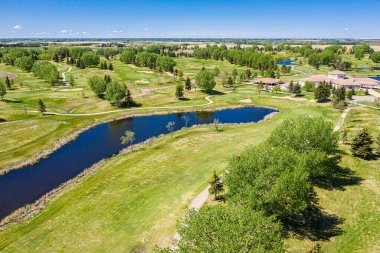 Arka planda ağaçlar ve gölcüklü golf sahası. Gölet çimenler ve ağaçlarla çevrili ve golf sahası kırsal bir alanda yer alıyor.
