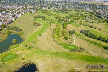 Arka planda gölet olan golf sahası. Gölet ağaçlar ve otlarla çevrilidir. Golf sahası büyük ve bakımlı.