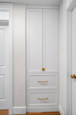 İki çekmeceli ve altın saplı beyaz dolap. Dolap uzun ve dar ve bir koridorda bulunuyor.