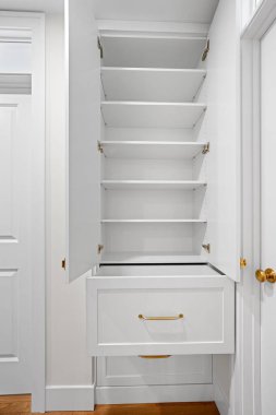 Rafları ve çekmecesi olan beyaz bir dolap. Dolap boş ve çekmecede altın sapı var.