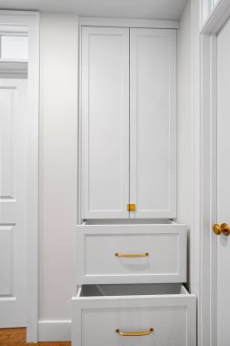 İki çekmeceli ve altın saplı beyaz dolap. Dolap boş ve minimalist bir görünümü var.