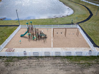Çocuk parkı ve çitleri olan bir park. Oyun parkında salıncak ve kaydırak var. Çit beyaz.