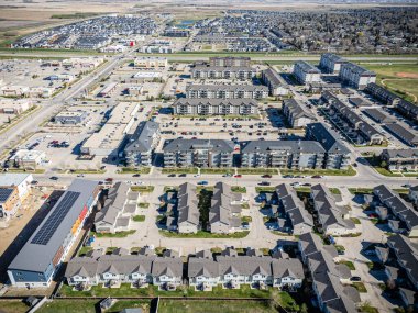 Bir sürü evi ve dairesi olan bir yerleşim yeri manzarası. Evler çoğunlukla beyaz ve daireler çoğunlukla kahverengi. Sokakta ve otoparklarda park edilmiş bir sürü araba var.