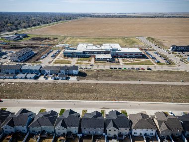 Arka planda büyük boş arsası olan bir yerleşim yeri. Evler küçük ve caddeye park edilmiş bir sürü araba var.