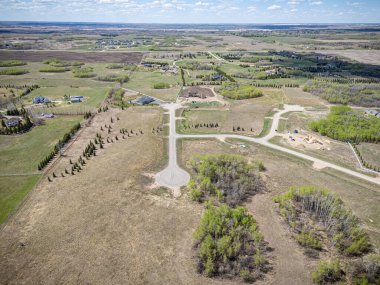Geniş, boş bir tarla ve birkaç ev uzakta. Evler dağılmış ve kırsal bir alanda gibi görünüyor.