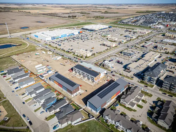 Şehir manzarası, ortasında büyük bir bina olan bir yerleşim alanı. Bina yapım aşamasında ve çatıda güneş paneli var. Bölgede park edilmiş bir sürü araba var.