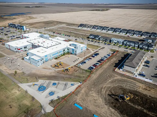 Çocuk parkı ve otoparkı olan büyük bir okul binası. Otopark arabalarla dolu ve okul çitlerle çevrili.