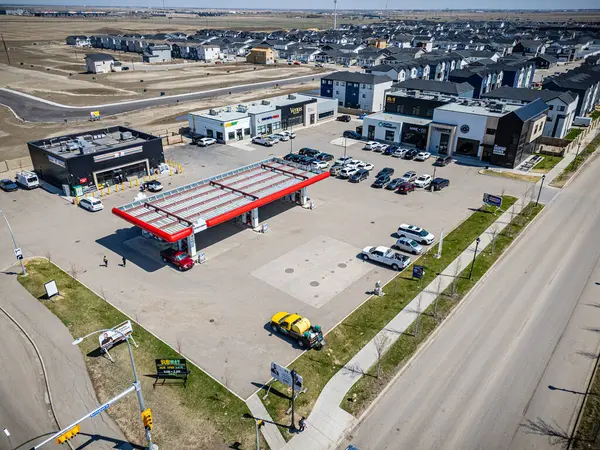 Önünde sarı bir kamyon olan benzin istasyonu. Benzin istasyonu birçok arabanın park edildiği bir otoparkla çevrilidir.