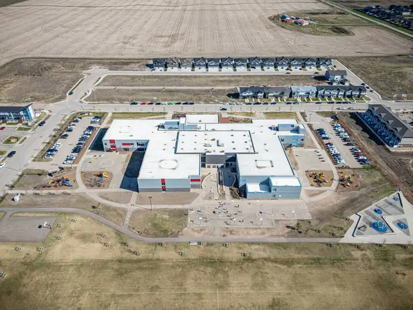 Okul yukarıdan gösteriliyor, otoparkı ve oyun alanı var. Okul büyük bir tarla ile çevrili ve otoparkta park edilmiş birkaç araba var. Sahne sakin ve huzurlu, okulla birlikte.