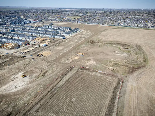 Arka planda büyük boş bir alan olan bir yerleşim alanı görüntüsü. Evlerin çoğu beyaz ve bölgede park etmiş birkaç araba var.
