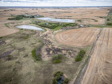 Geniş bir arazi, birkaç küçük gölet ve uzakta birkaç ev. Gökyüzü bulutlu ve toprak kuru.