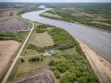 Nehir, kıyıda yeşil bir evi olan kırsal bir bölgeden geçiyor. Ev ağaçlarla çevrili ve nehir sakin.