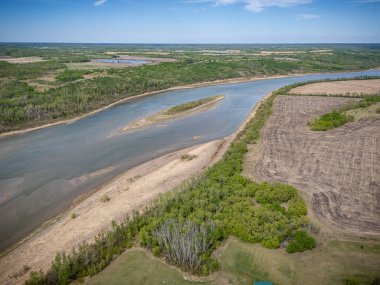 Kumlu bir kıyı şeridi ve diğer tarafında orman olan bir nehir. Gökyüzü açık ve mavi