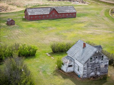 Ahırın yanındaki tarlada küçük bir ev var. Ahır eski ve ev de eski. Çimler yeşil, gökyüzü mavi.
