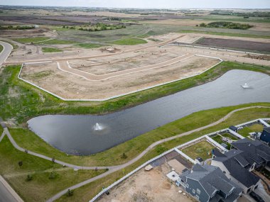 Geniş bir su kütlesi ve beyaz çitleri olan yerleşim yeri manzarası. Su çimenler ve ağaçlarla çevrili ve arka planda birkaç ev var.