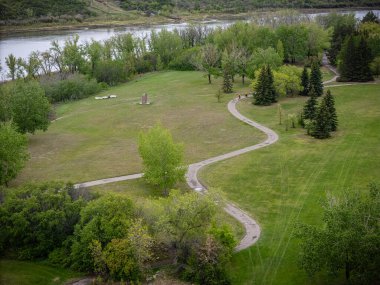 Bir patika ve ağaçla park et. Yol kıvrımlı ve çimenler yeşil. Yolda yürüyen insanlar var.