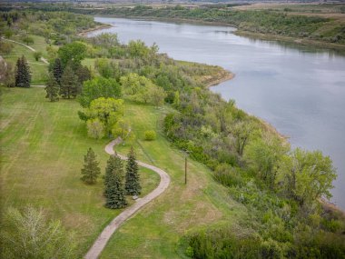 Nehir ağaçlar ve çimlerle dolu bir parktan geçiyor. Su sakin, ağaçlar yeşil.