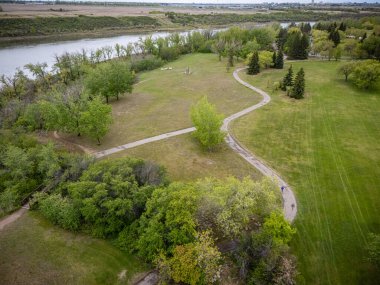 Arka planda nehir ve patika olan bir park yeri. Yol ağaçlar ve otlarla çevrili.