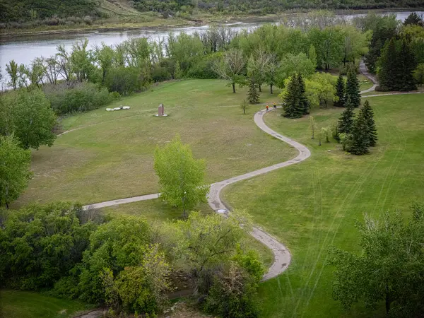 Bir patika ve ağaçla park et. Yol kıvrımlı ve çimenler yeşil. Yolda yürüyen insanlar var.