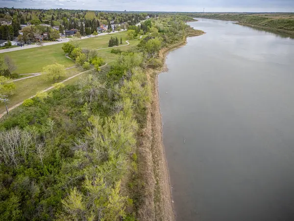 Nehir, arka planda bir kasaba olan ormanlık bir bölgeden geçiyor. Su sakin, ağaçlar yemyeşil.