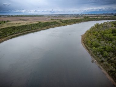 Yeşil bir kıyısı ve arka planında bulutlu bir gökyüzü olan bir nehir. Su sakin ve gökyüzü kapalı.