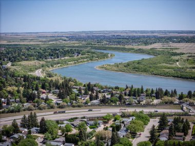 İçinden nehir akan bir şehir. Nehir ağaçlar ve evlerle çevrilidir. Evler dağılmış ve yolda arabalar var.