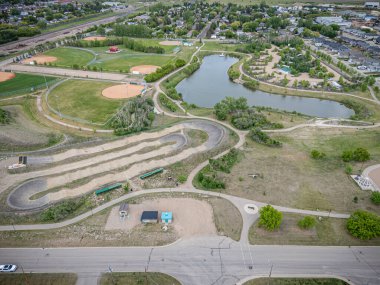 Toprak yolu ve göleti olan bir park. Park evlerle çevrilidir. Gökyüzü mavi