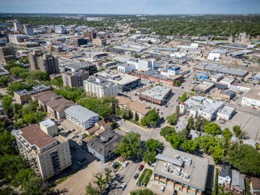 Görüntü yukarıdan bir şehrin panoramik bir görüntüsü, şehir manzarasını oluşturan çeşitli binaları ve ağaçları gösteriyor. Şehir konut ve ticari alanların karışımı gibi görünüyor.
