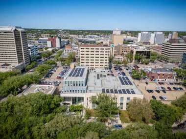 Şehir manzarası ve ortasında büyük bir bina. Binanın çatısında güneş panelleri var.