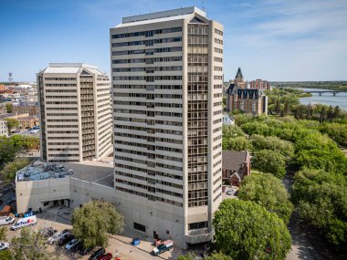 Önünde bir sürü pencere ve yeşil bir ağaç olan büyük bir bina. Bina arabalar ve bir köprü ile çevrili.