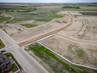 Toprak yolu ve çiti olan bir şantiye manzarası. Yol ağaçlarla kaplı ve çitler beyaz.