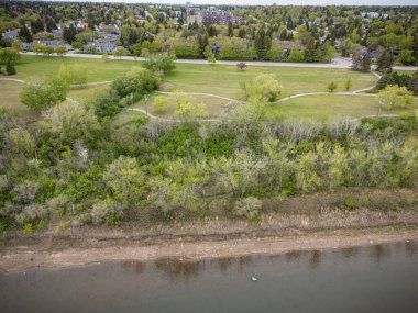 İçinden nehir akan bir park manzarası. Park ağaçlar ve evlerle çevrili.