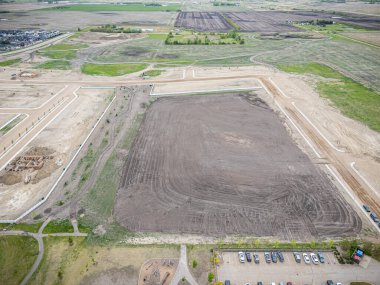 Ortasında toprak yol olan geniş bir arazi. Yol çitlerle çevrili ve park yerinde birkaç araba var.