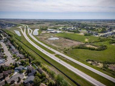 Birden fazla şeritli ve üzerinde bir sürü araba olan bir otoyol. Yol, bir banliyö bölgesi izlenimi veren evler ve birkaç binayla çevrili. Gökyüzü açık ve güneş parlıyor.