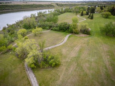 Arka planda nehir ve patika olan bir park yeri. Yol ağaçlar ve otlarla çevrili.