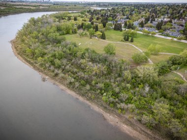 Nehir arka planda küçük bir kasaba olan ormanlık bir bölgeden geçiyor. Su sakin, ağaçlar yemyeşil.