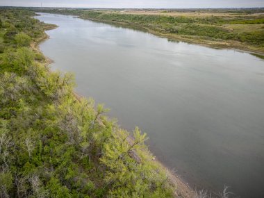 Kıyısında ağaçlar olan bir nehir. Su sakin ve berrak. Ağaçlar yeşil ve yemyeşil.