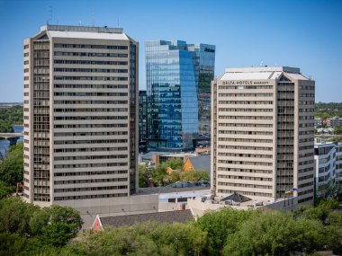 Cam cepheli ve arka planda büyük bir otel olan iki uzun bina. Gökyüzü açık ve güneş parlıyor.