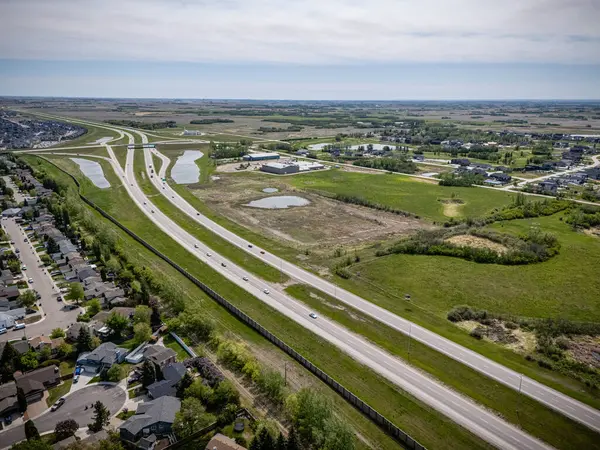 Birden fazla şeritli ve üzerinde bir sürü araba olan bir otoyol. Yol, bir banliyö bölgesi izlenimi veren evler ve birkaç binayla çevrili. Gökyüzü açık ve güneş parlıyor.