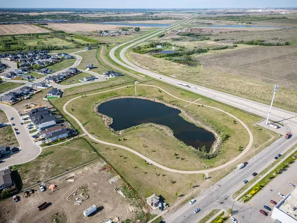 Ortasında gölet olan geniş, açık bir alan. Gölet ağaçlar ve otlarla çevrilidir. Gökyüzü açık ve güneş parlıyor.