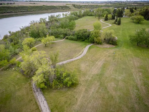 Arka planda nehir ve patika olan bir park yeri. Yol ağaçlar ve otlarla çevrili.