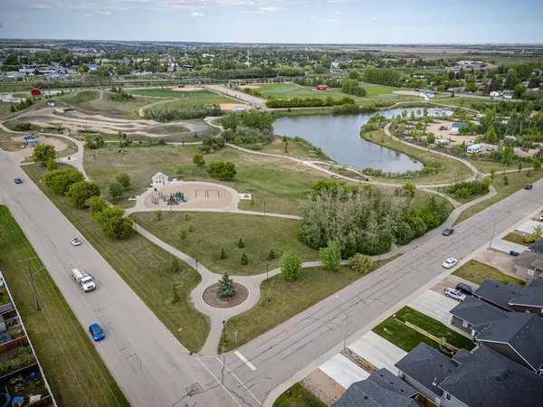 Göleti ve oyun parkı olan bir park. Park evler ve bir yol ile çevrilidir. Gökyüzü bulutlu.