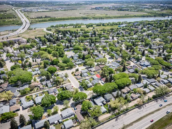 Evleri ve ağaçları olan bir yerleşim yeri. Evlerin çoğu beyaz ve ağaçlar yeşil. Yolda arabalar ve arka planda bir nehir var.