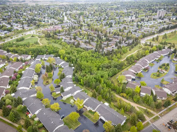 Evleri ve ağaçları olan bir yerleşim alanı. Evlerin çoğu beyaz ve caddelerde park edilmiş birçok araba var. Gökyüzü bulutlu ve görüntünün genel havası sakin ve huzurlu.