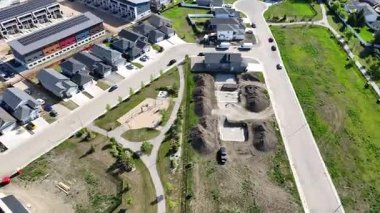 Evleri ve parkı olan bir yerleşim yeri. Parkın bir oyun alanı ve basketbol sahası var. Sokağa park etmiş bazı arabalar da var.