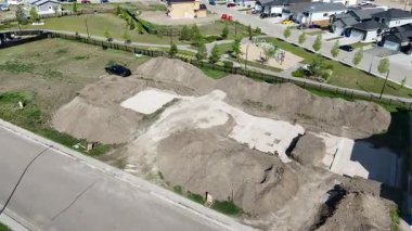 Kirli bir arazisi ve bir yığın toprağı olan bir yerleşim yeri. Kirli arazi bir caddenin yanında ve caddeye park edilmiş bazı arabalar var.