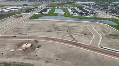 Toprak yolu ve küçük bir binası olan bir şantiye manzarası. Yol bir çitle çevrili ve yol boyunca park edilmiş birkaç araba var.