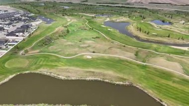 Arka planda gölet olan golf sahası. Gölet çimenler ve ağaçlarla çevrilidir. Golf sahası yerleşim bölgesinde.